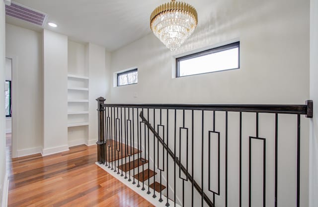 hallway with hardwood / wood-style floors, a notable chandelier, and built in shelves