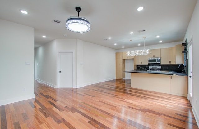 kitchen featuring pendant lighting, appliances with stainless steel finishes, tasteful backsplash, light brown cabinets, and light wood-type flooring