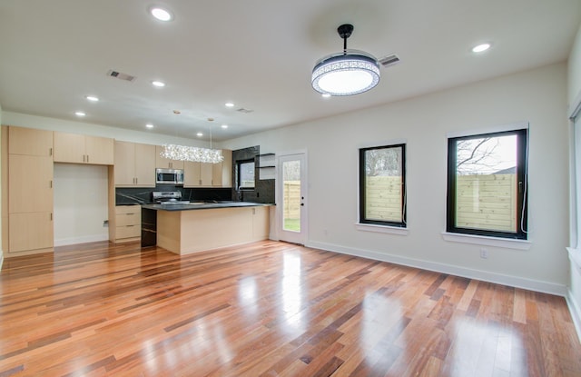 kitchen with pendant lighting, decorative backsplash, stainless steel appliances, and light hardwood / wood-style flooring