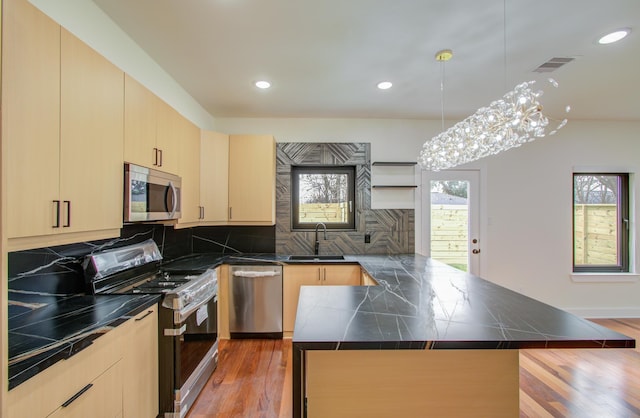 kitchen featuring sink, decorative light fixtures, light brown cabinets, appliances with stainless steel finishes, and a kitchen island