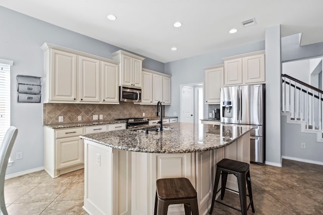 kitchen with sink, dark stone counters, an island with sink, and appliances with stainless steel finishes