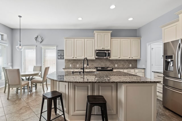 kitchen with pendant lighting, an island with sink, sink, stainless steel appliances, and cream cabinets