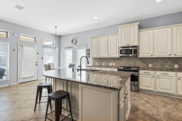 kitchen featuring pendant lighting, sink, appliances with stainless steel finishes, backsplash, and an island with sink