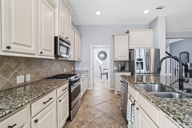 kitchen featuring white cabinets, stainless steel appliances, sink, and dark stone counters