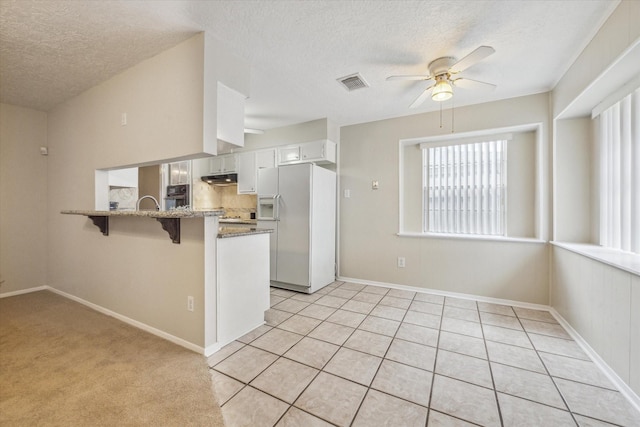 kitchen featuring black oven, white cabinetry, light stone countertops, white fridge with ice dispenser, and kitchen peninsula