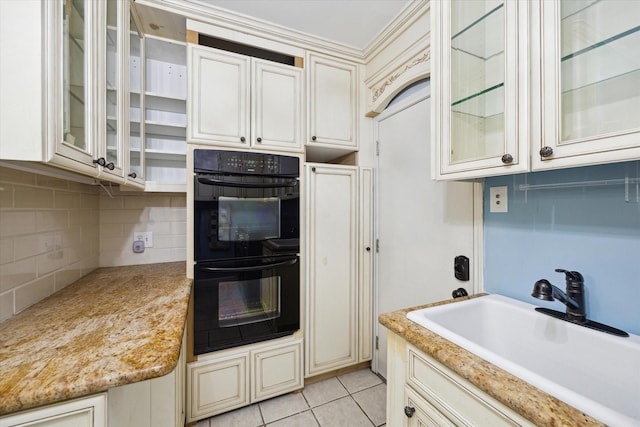 kitchen with sink, light tile patterned floors, backsplash, black double oven, and cream cabinetry