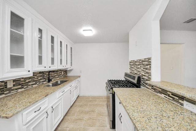 kitchen with sink, stainless steel gas range oven, light stone countertops, and white cabinets