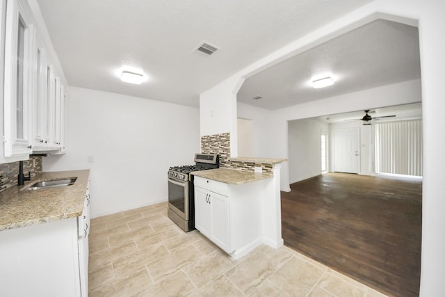 kitchen featuring sink, ceiling fan, backsplash, stainless steel gas range oven, and white cabinets