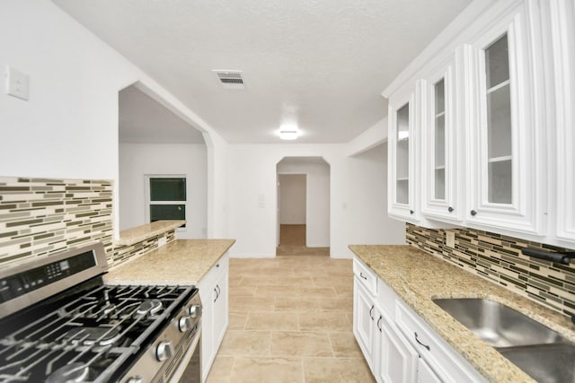 kitchen featuring sink, stainless steel gas range, backsplash, light stone counters, and white cabinets