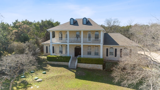 view of front facade with a front lawn, a balcony, and a porch