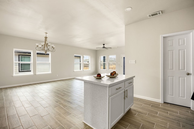 kitchen featuring pendant lighting, ceiling fan with notable chandelier, a center island, and white cabinets