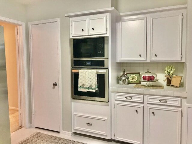 kitchen with tasteful backsplash, tile countertops, oven, and white cabinets