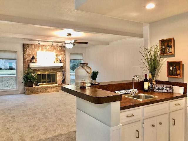 kitchen featuring sink, kitchen peninsula, carpet floors, a fireplace, and white cabinets