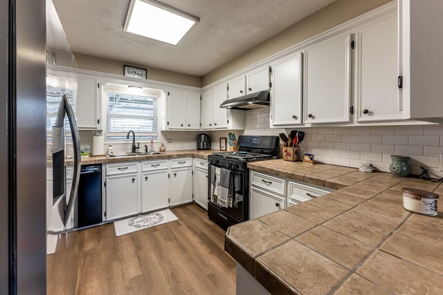 kitchen with tasteful backsplash, white cabinetry, sink, and black appliances