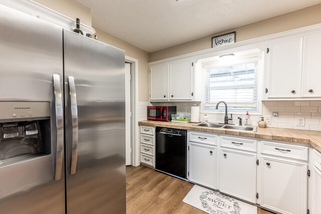 kitchen with white cabinetry, dishwasher, sink, stainless steel fridge, and light hardwood / wood-style floors