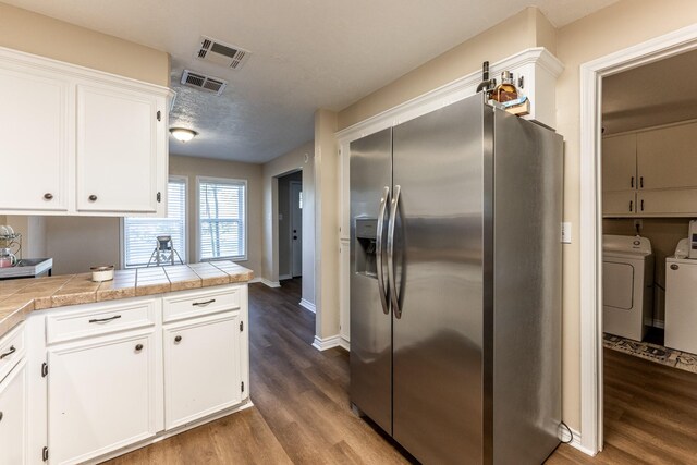 kitchen featuring stainless steel refrigerator with ice dispenser, white cabinetry, washer and dryer, tile counters, and dark hardwood / wood-style flooring