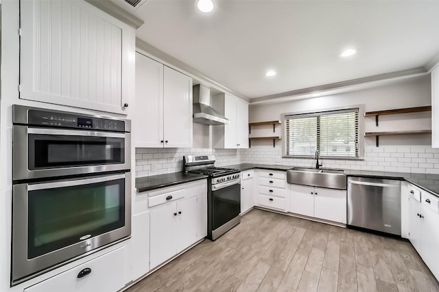 kitchen featuring sink, white cabinetry, appliances with stainless steel finishes, decorative backsplash, and wall chimney range hood