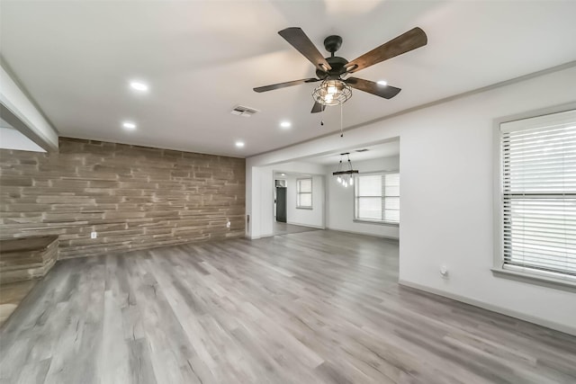 unfurnished living room with ceiling fan with notable chandelier and light hardwood / wood-style floors