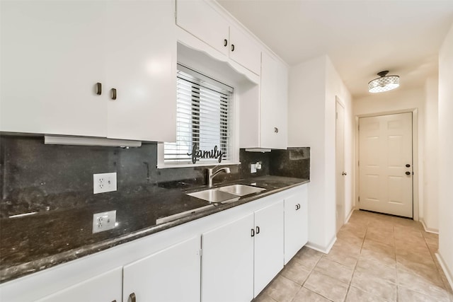 kitchen featuring sink, light tile patterned floors, white cabinetry, backsplash, and dark stone counters