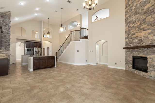 kitchen featuring dark brown cabinets, hanging light fixtures, a center island with sink, stainless steel appliances, and a fireplace