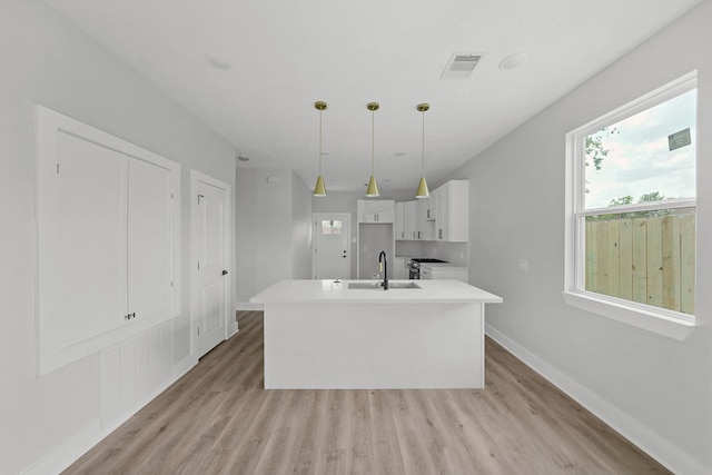 kitchen featuring decorative light fixtures, sink, white cabinets, light hardwood / wood-style floors, and a center island with sink