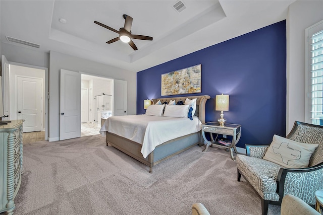 bedroom featuring ceiling fan, light colored carpet, connected bathroom, and a raised ceiling