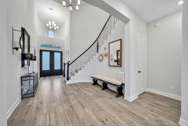 foyer entrance with a towering ceiling, light wood-type flooring, and a notable chandelier