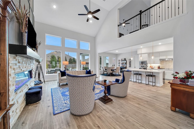 living room featuring a stone fireplace, sink, high vaulted ceiling, ceiling fan, and light hardwood / wood-style floors