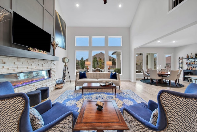 living room featuring ceiling fan, high vaulted ceiling, a fireplace, and light hardwood / wood-style floors