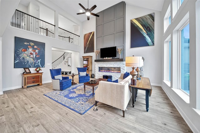 living room featuring light wood-type flooring, a towering ceiling, a fireplace, and plenty of natural light