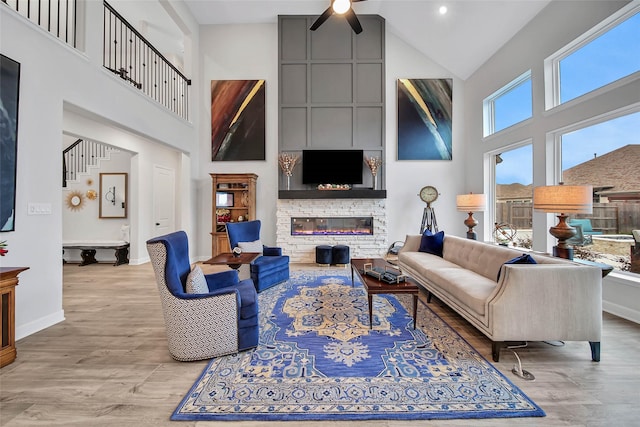 living room with a stone fireplace, high vaulted ceiling, and light wood-type flooring