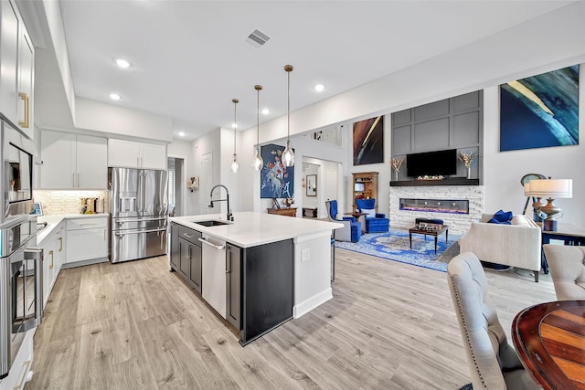 kitchen with sink, a kitchen island with sink, hanging light fixtures, stainless steel appliances, and white cabinets