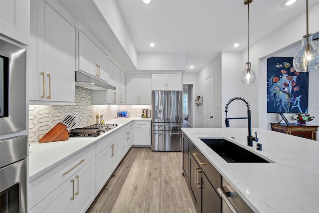 kitchen with pendant lighting, sink, appliances with stainless steel finishes, light stone counters, and white cabinets