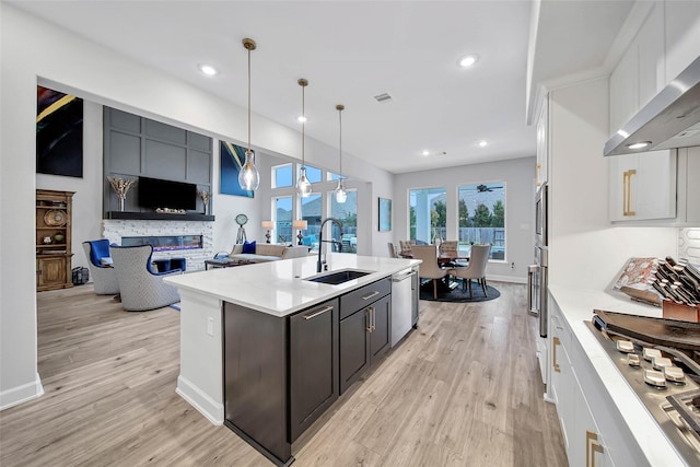 kitchen with sink, hanging light fixtures, appliances with stainless steel finishes, white cabinets, and wall chimney range hood