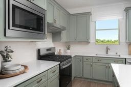 kitchen with under cabinet range hood, wood finished floors, a sink, light countertops, and appliances with stainless steel finishes