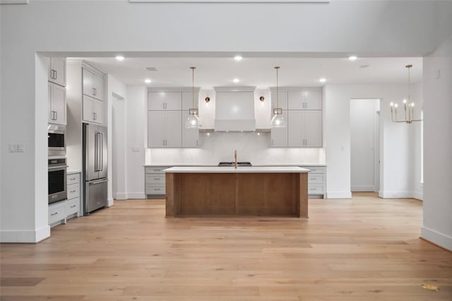 kitchen featuring decorative light fixtures, decorative backsplash, stainless steel appliances, a center island with sink, and light hardwood / wood-style flooring