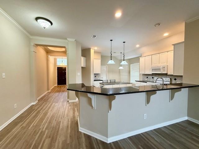 kitchen featuring pendant lighting, kitchen peninsula, white cabinets, and a kitchen bar