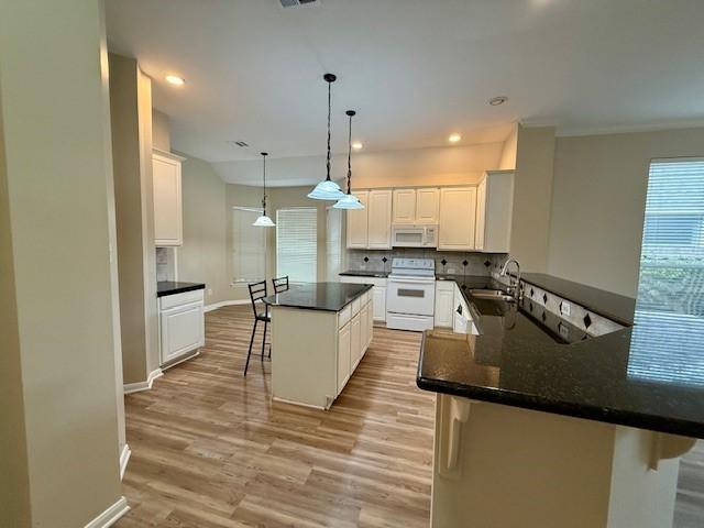 kitchen with white cabinetry, white appliances, a kitchen breakfast bar, and kitchen peninsula