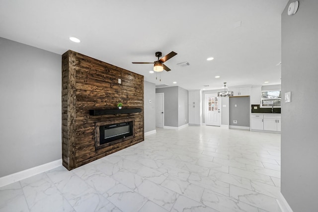 unfurnished living room with a large fireplace, sink, and ceiling fan with notable chandelier