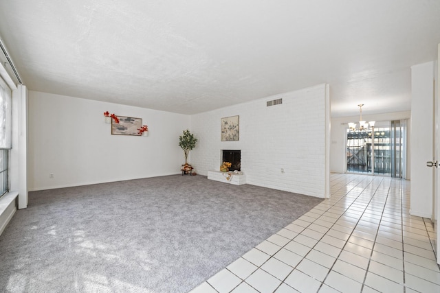 unfurnished living room featuring an inviting chandelier, a fireplace, a textured ceiling, brick wall, and light carpet