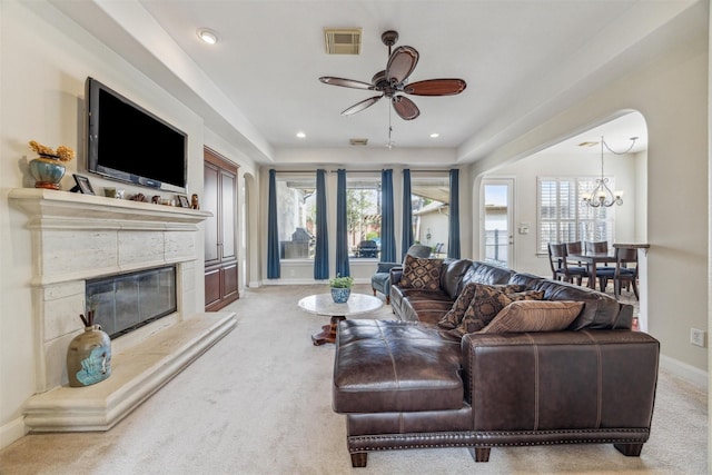 living room with light colored carpet, a high end fireplace, and ceiling fan with notable chandelier