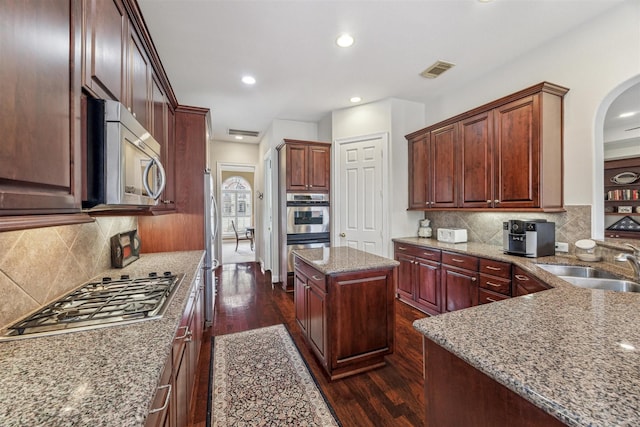 kitchen featuring stainless steel appliances, light stone countertops, a center island, and sink