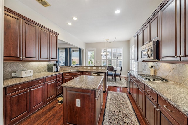 kitchen with sink, appliances with stainless steel finishes, hanging light fixtures, dark hardwood / wood-style floors, and a center island