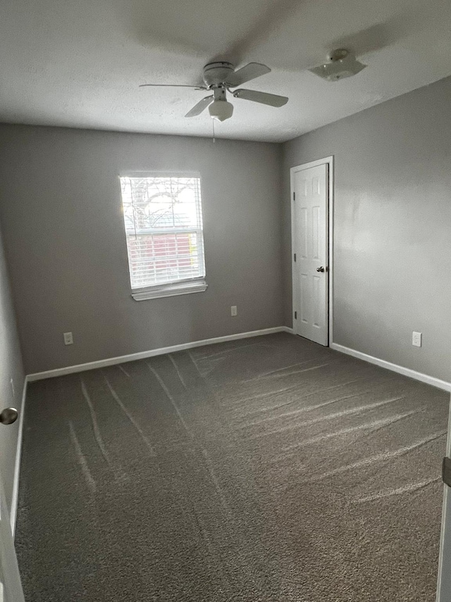 spare room featuring dark colored carpet and ceiling fan