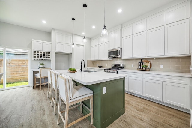 kitchen with appliances with stainless steel finishes, pendant lighting, sink, white cabinets, and a center island with sink