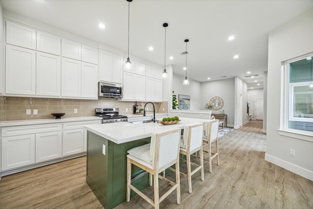 kitchen with pendant lighting, white cabinetry, stainless steel appliances, a kitchen breakfast bar, and an island with sink