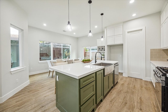 kitchen with sink, appliances with stainless steel finishes, white cabinetry, green cabinets, and an island with sink