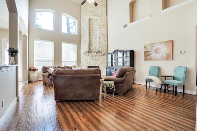 living room with a high ceiling, dark hardwood / wood-style flooring, ceiling fan, and a fireplace