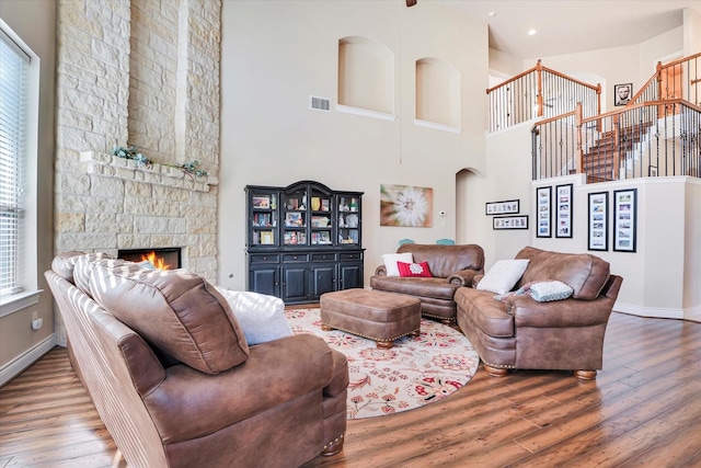 living room with hardwood / wood-style flooring, a stone fireplace, and a high ceiling