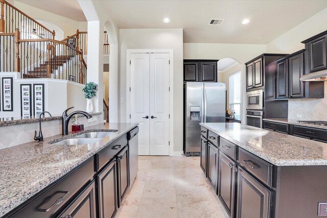 kitchen featuring appliances with stainless steel finishes, tasteful backsplash, sink, light stone counters, and a center island with sink